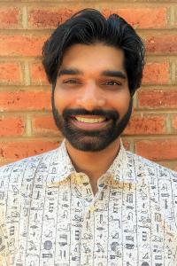 A smiling bearded man with a brick wall background